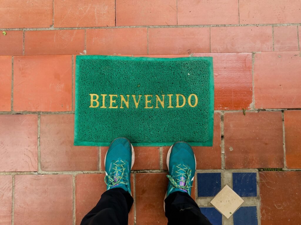 Aerial view of a green welcome doormat with 'Bienvenido' against a tiled floor with shoes visible.